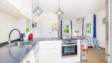 A modern kitchen with a built-in oven, a sink, and a countertop. There is a small dining area with a table and chairs.