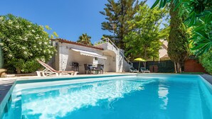 Una piscina con sillas de descanso, un porche cubierto y un edificio de fachada blanca.