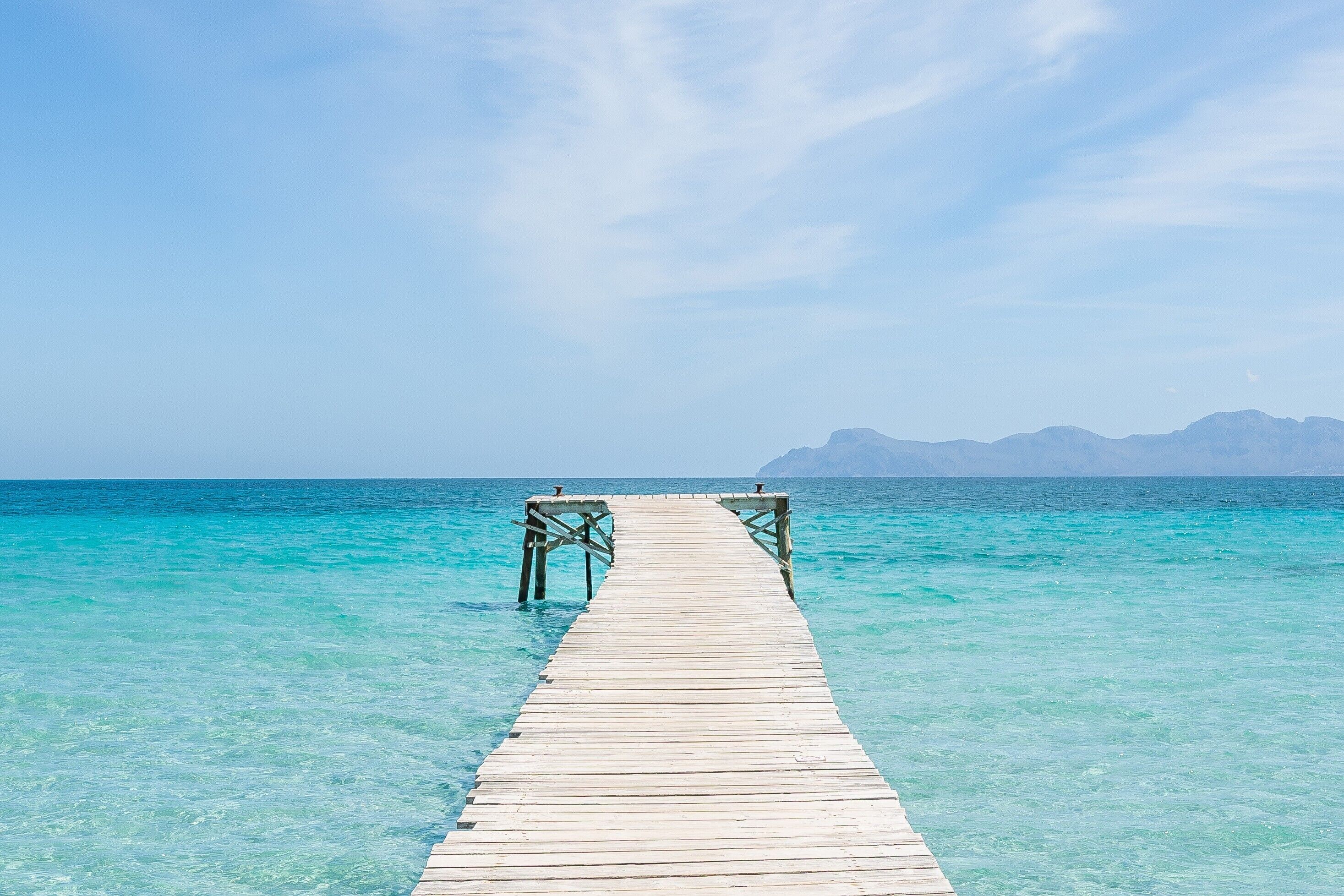 Un muelle de madera que se adentra en aguas turquesas cristalinas, con montañas al fondo.