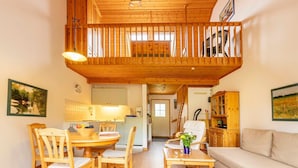 A wooden-floored living area with a dining table, chairs, a sofa, and a balcony with a railing. - Vacation home Milan, terraced house center, 2 (+2) persons 001 - Feriendorf Müritzufer (Rechlin)