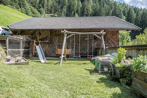 A rustic wooden building with a tiled roof, a swing set, and a fenced area with a cat.