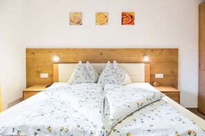 A bed with a floral bedspread, wooden headboard, bedside tables, and wall-mounted lights.