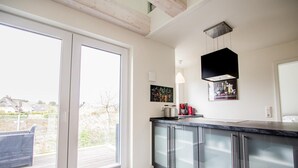 Una cocina moderna con puerta de cristal que da a un balcón, armarios de acero inoxidable y una lámpara colgante.
