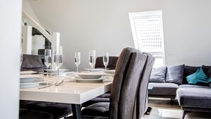 Un comedor con una mesa preparada para cuatro personas, una silla tapizada de gris y un sofá de color gris al fondo.