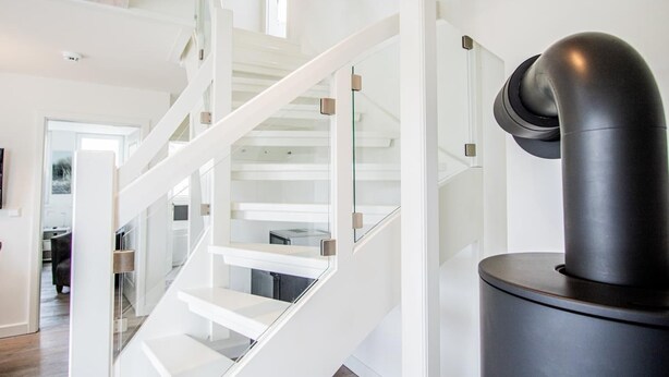 Una escalera moderna con barandillas de vidrio y un objeto cilíndrico negro a la derecha.