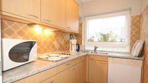 A compact kitchen with wooden cabinets, a microwave, a coffee maker, and a dishwasher. - Bangert House Cäcilia (Wenningstedt-Braderup (Sylt))
