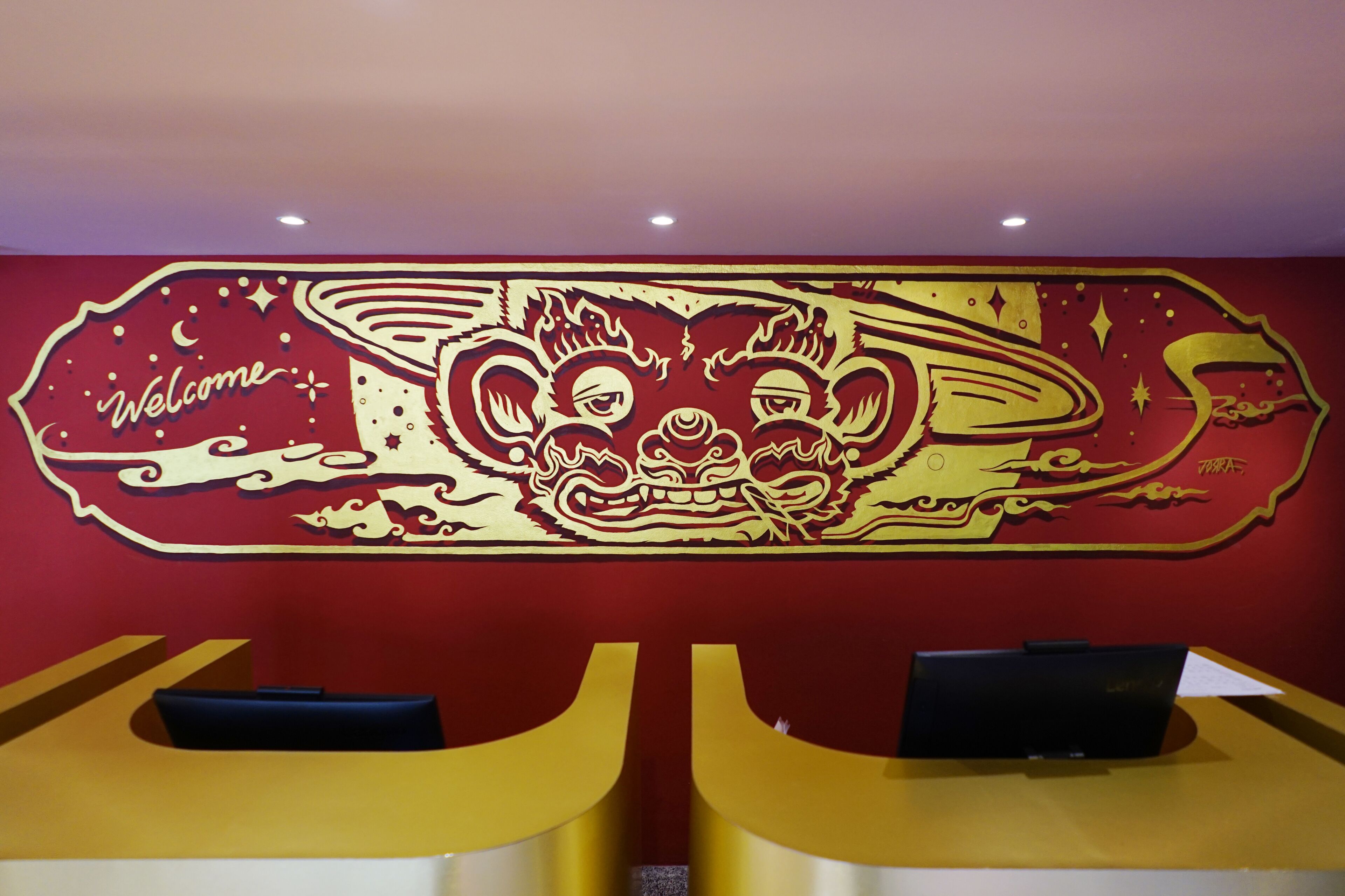Un mostrador de recepción con un mural decorativo en rojo y dorado.