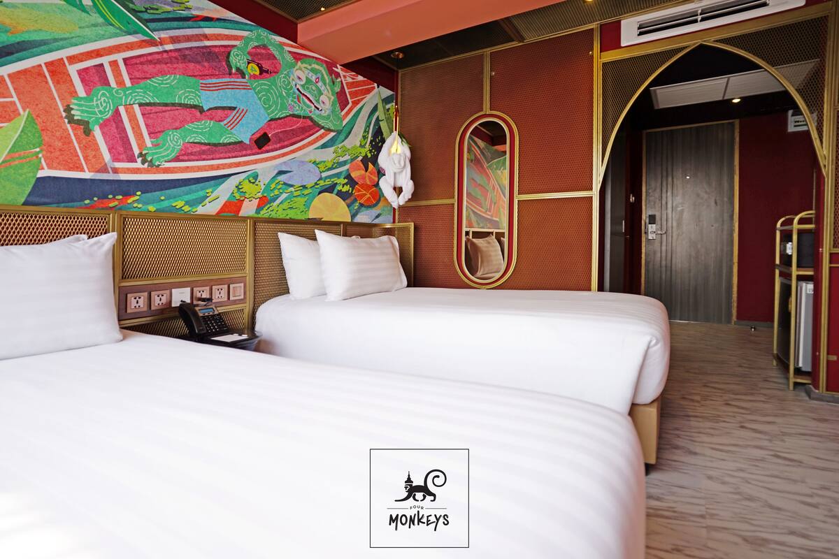 Habitación de hotel con dos camas, un mural colorido, un espejo y piso de madera.