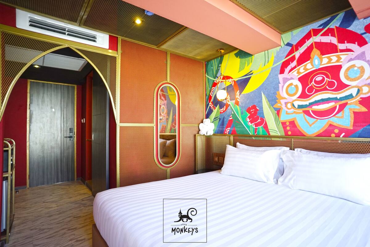 Habitación de hotel con cama, espejo, un mural colorido y una puerta que da a otra habitación.