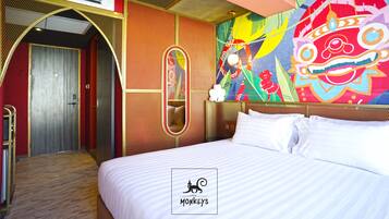Une chambre d’hôtel avec un lit, un miroir, une fresque murale colorée et une porte donnant sur une autre pièce.