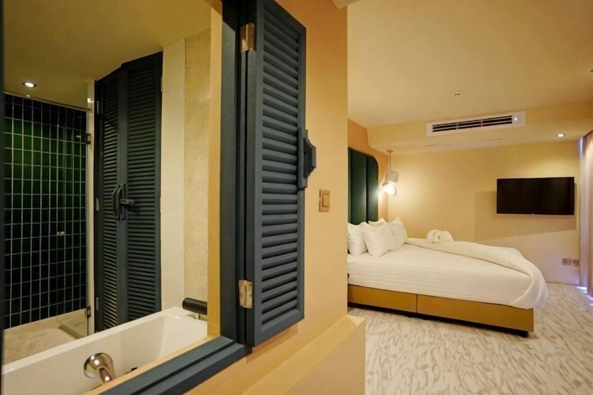 Una habitación de hotel con una cama grande, una bañera y un televisor montado en la pared.