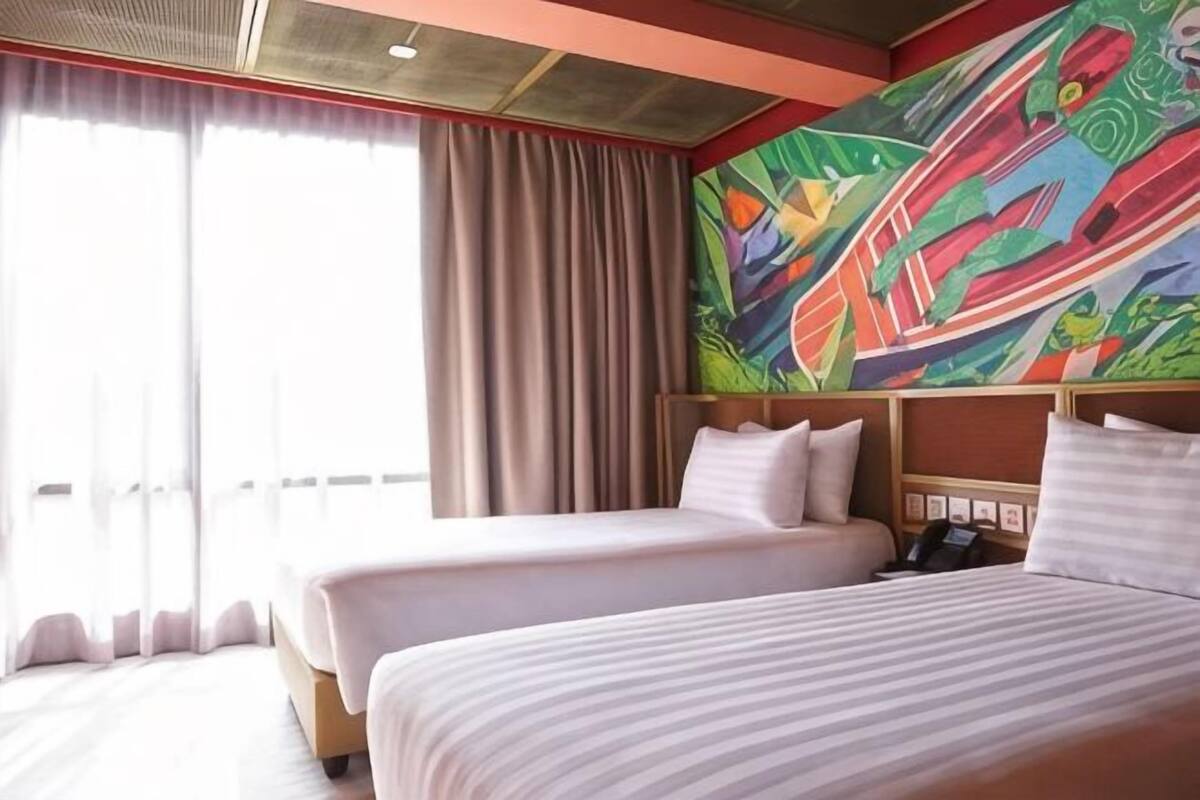 Habitación de hotel con dos camas, un ventanal con cortinas y un cuadro abstracto colorido en la pared.