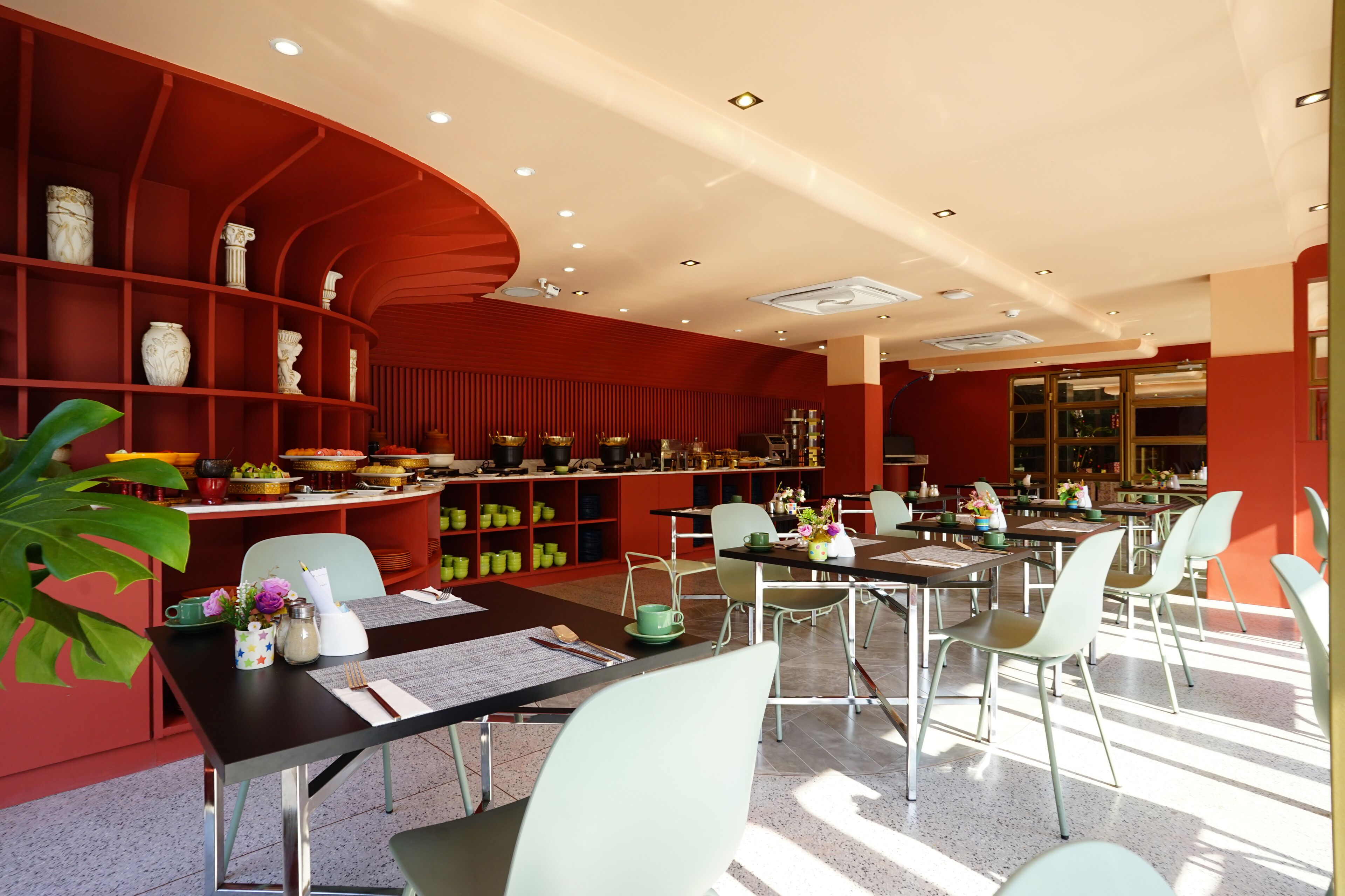 Un comedor moderno con estanterías rojas, sillas verdes y una variedad de platos exhibidos en las estanterías.