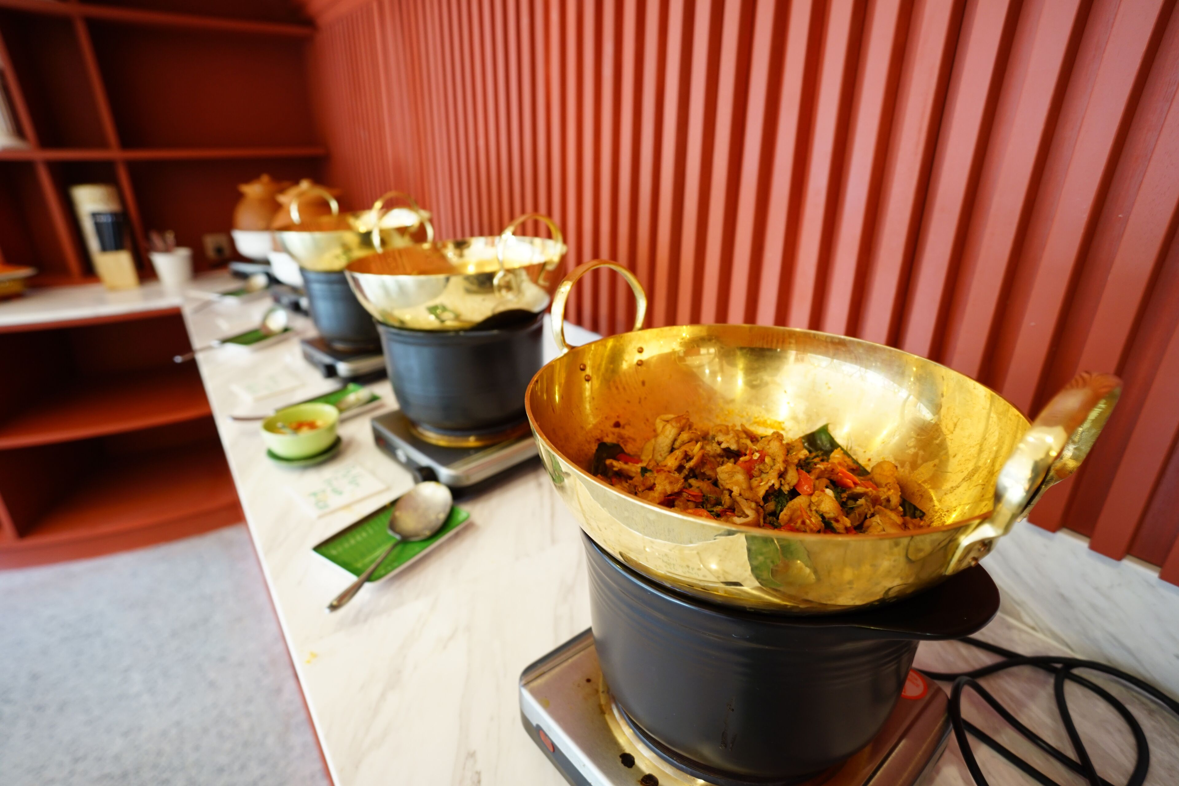 Una encimera de cocina con varias ollas y sartenes doradas, algunas con comida, y algunos utensilios como palillos y una cuchara.