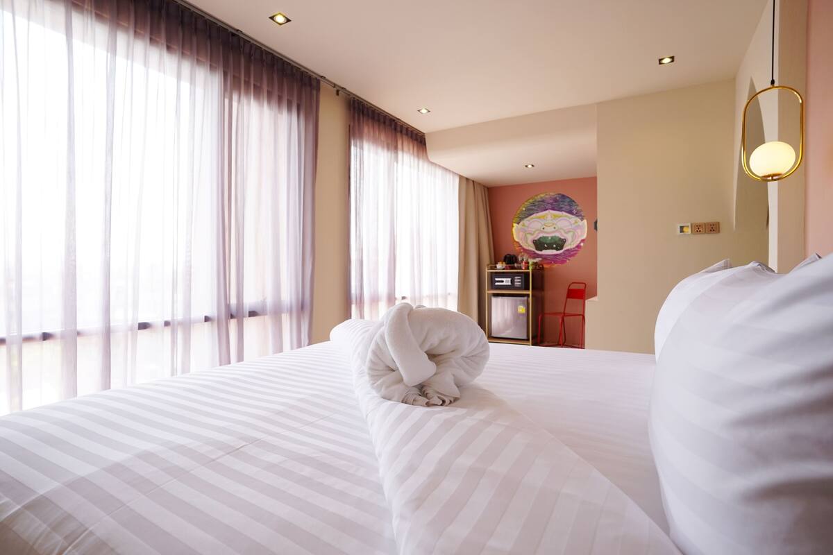 Una habitación de hotel con una cama grande, un escritorio con una computadora y un ventanal con cortinas.
