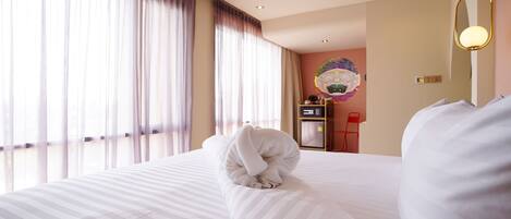 A hotel room with a large bed, a desk with a computer, and a window with curtains.
