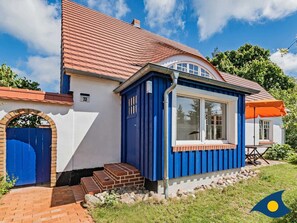 A house with a red-tiled roof, a blue door, and a small porch with steps leading to the entrance.
