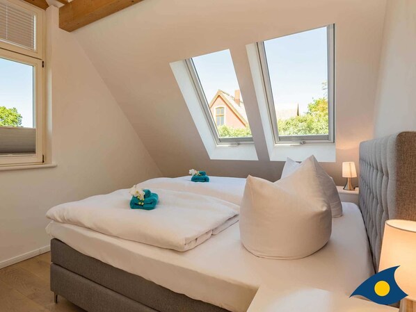 A bedroom with a bed, pillows, a bedside table with a lamp, and two skylights.