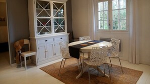 Ein Essbereich mit weißem Tisch und Stühlen, einem Schrank mit Glastüren und einem Fenster mit Vorhängen.