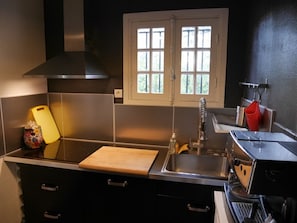 Una cocina moderna con encimera de acero inoxidable, tabla de cortar de madera, pileta y cafetera.