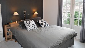 Ein Schlafzimmer mit einem großen Bett, zwei Nachttischlampen, einem Nachttisch und einem Fenster mit Vorhängen.