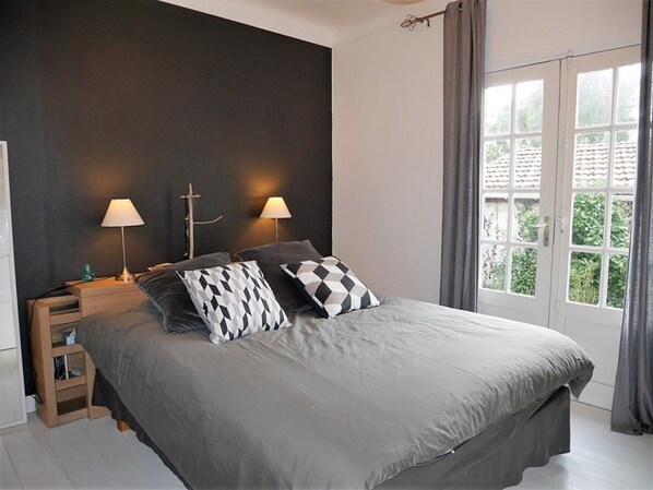 Un dormitorio con una cama grande, dos lámparas de noche, una mesita de noche y una ventana con cortinas.
