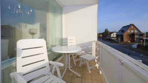 A balcony with a white table and chairs, a glass door, and a view of a street and houses. - Sylt breeze <br>Wenningstedt on the beach (Wenningstedt)