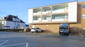 A modern building with multiple floors, a parking area, and a white car parked in front. - Sylt breeze <br>Wenningstedt on the beach (Wenningstedt)