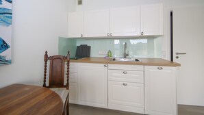 A compact kitchen with white cabinets, a wooden dining table, and a chair. - Sylt breeze <br>Wenningstedt on the beach (Wenningstedt)