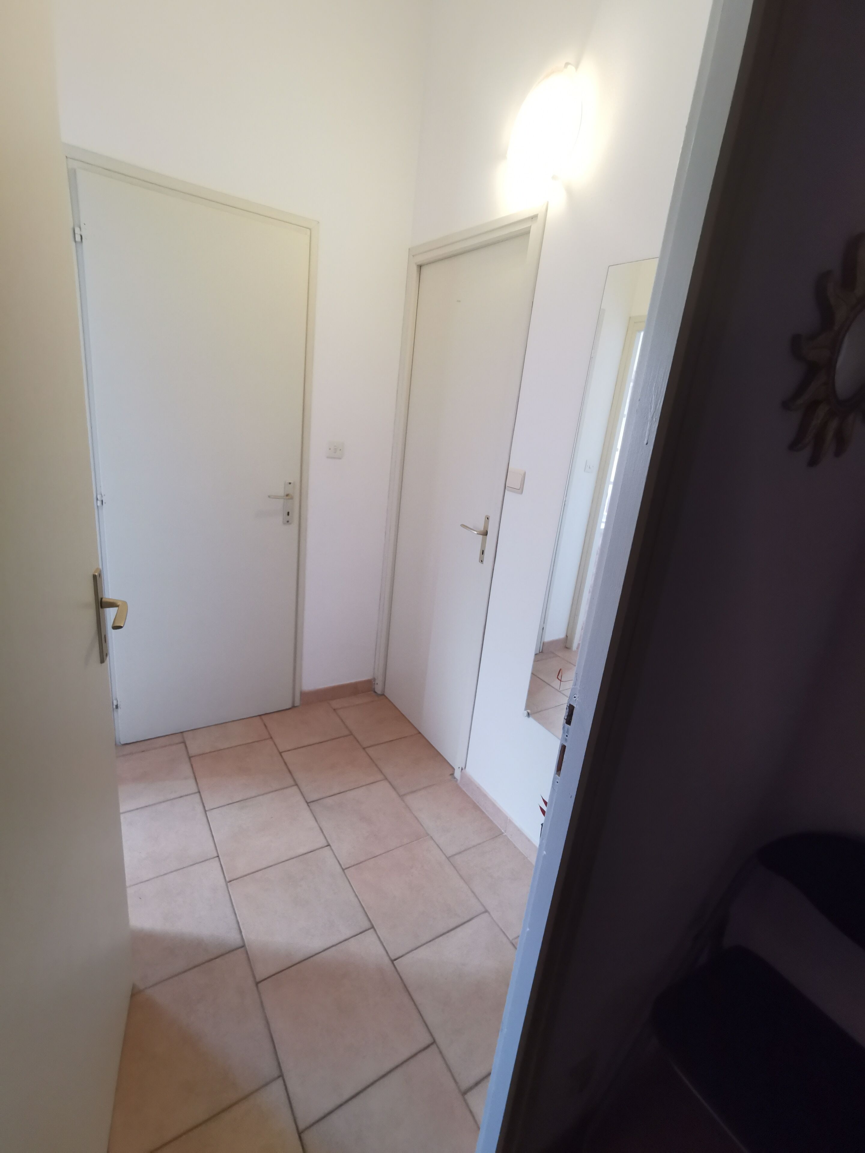 A hallway with two white doors, a light fixture above the right door, and a tiled floor.