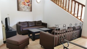 A living room with a sofa, ottoman, coffee table, and a TV on a stand. - Semi-detached Villa Sea View - Private Parking - Near Town Center and Beaches (Propriano)