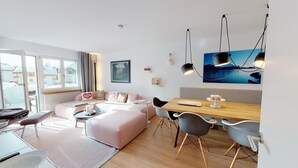 Una sala de estar moderna con un sofá, una mesa de comedor y sillas. Hay una ventana que ofrece vistas a edificios.