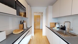 Una cocina estrecha con armarios blancos, encimera de madera, un fregadero y una cafetera.