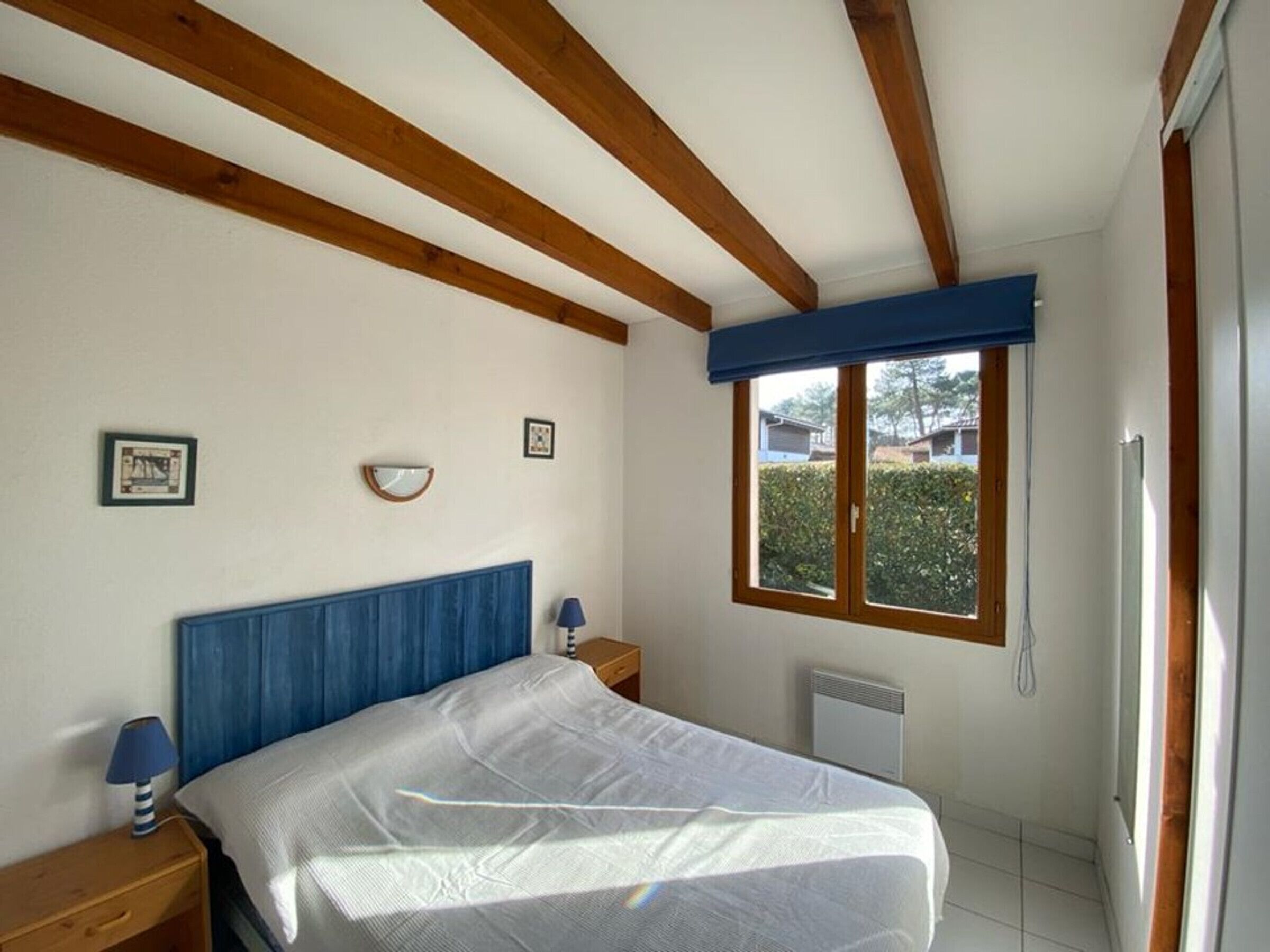Une chambre à coucher avec un lit, des poutres en bois, une fenêtre et un radiateur.