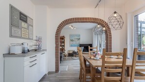 A modern kitchen with a brick archway leading to a dining area, featuring a wooden table and chairs, a coffee machine, and a bookshelf.