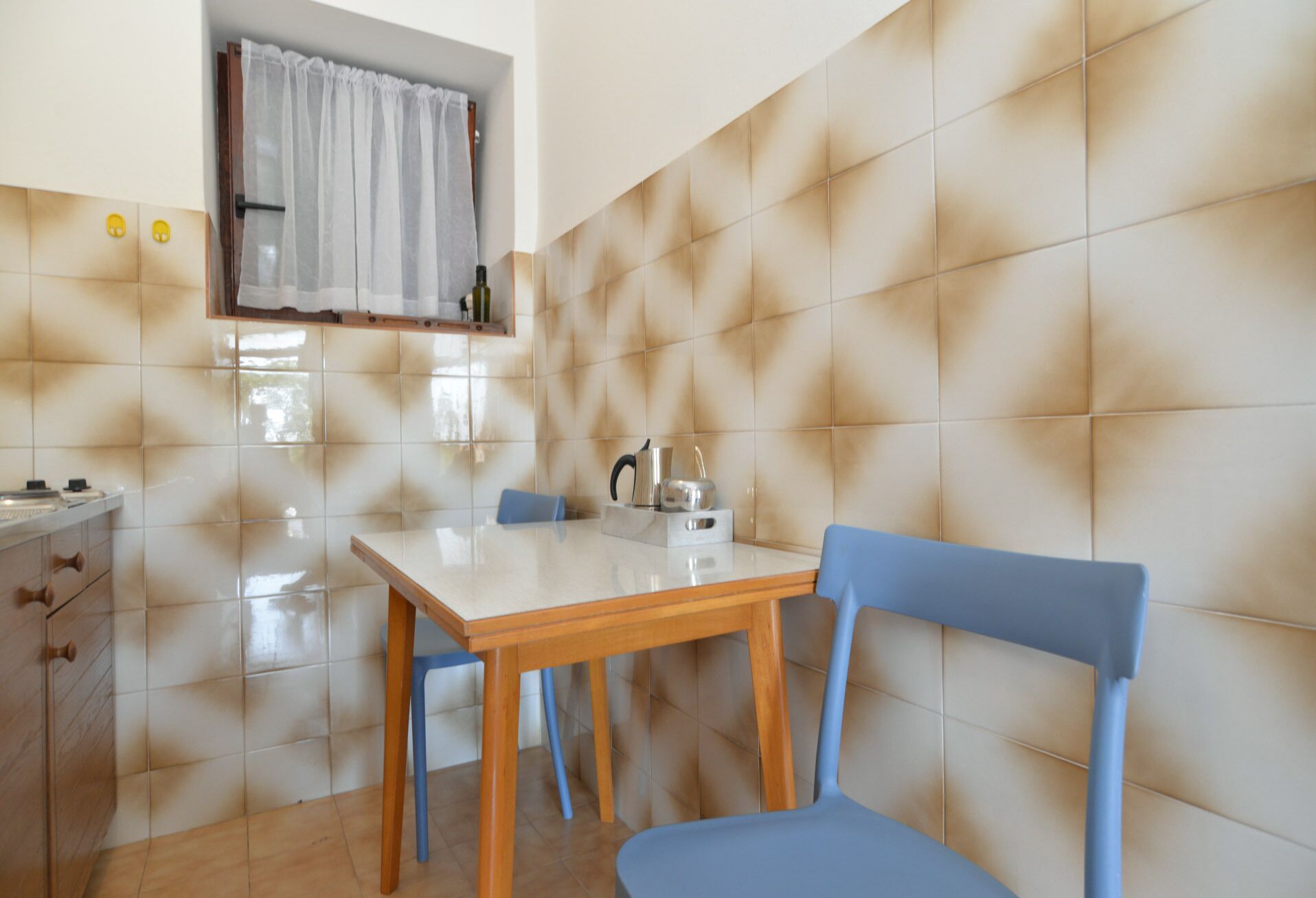 A small kitchen with a tiled backsplash, a wooden table, and blue chairs.