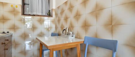 A small kitchen with a tiled backsplash, a wooden table, and blue chairs.
