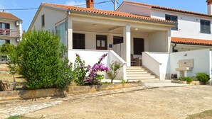 Une maison moderne à deux étages, dotée d’un porche abrité, d’un escalier menant à l’étage supérieur et d’un petit jardin agrémenté de plantes à fleurs.