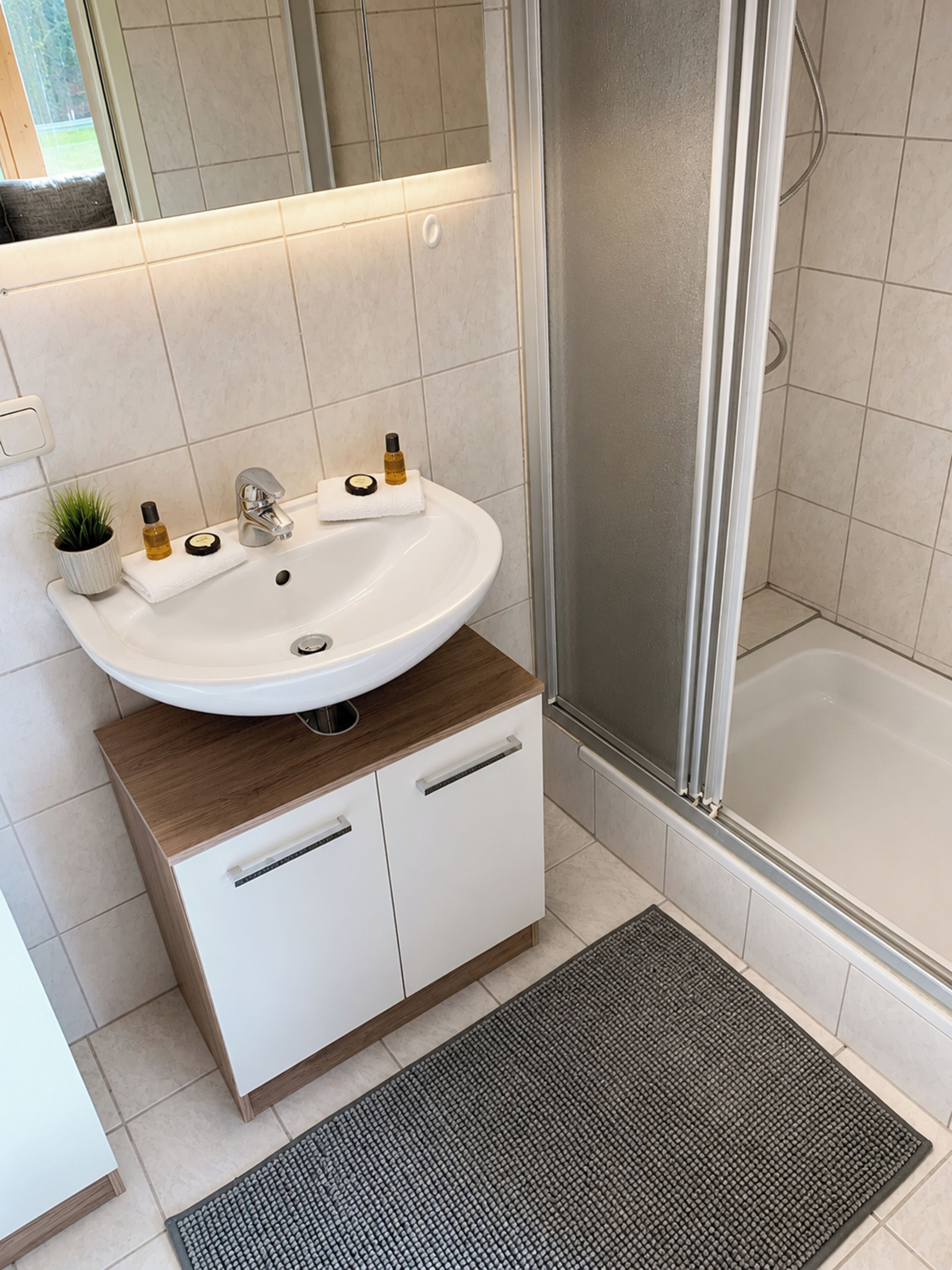 A bathroom with a white sink, wooden cabinet, and a shower area.
