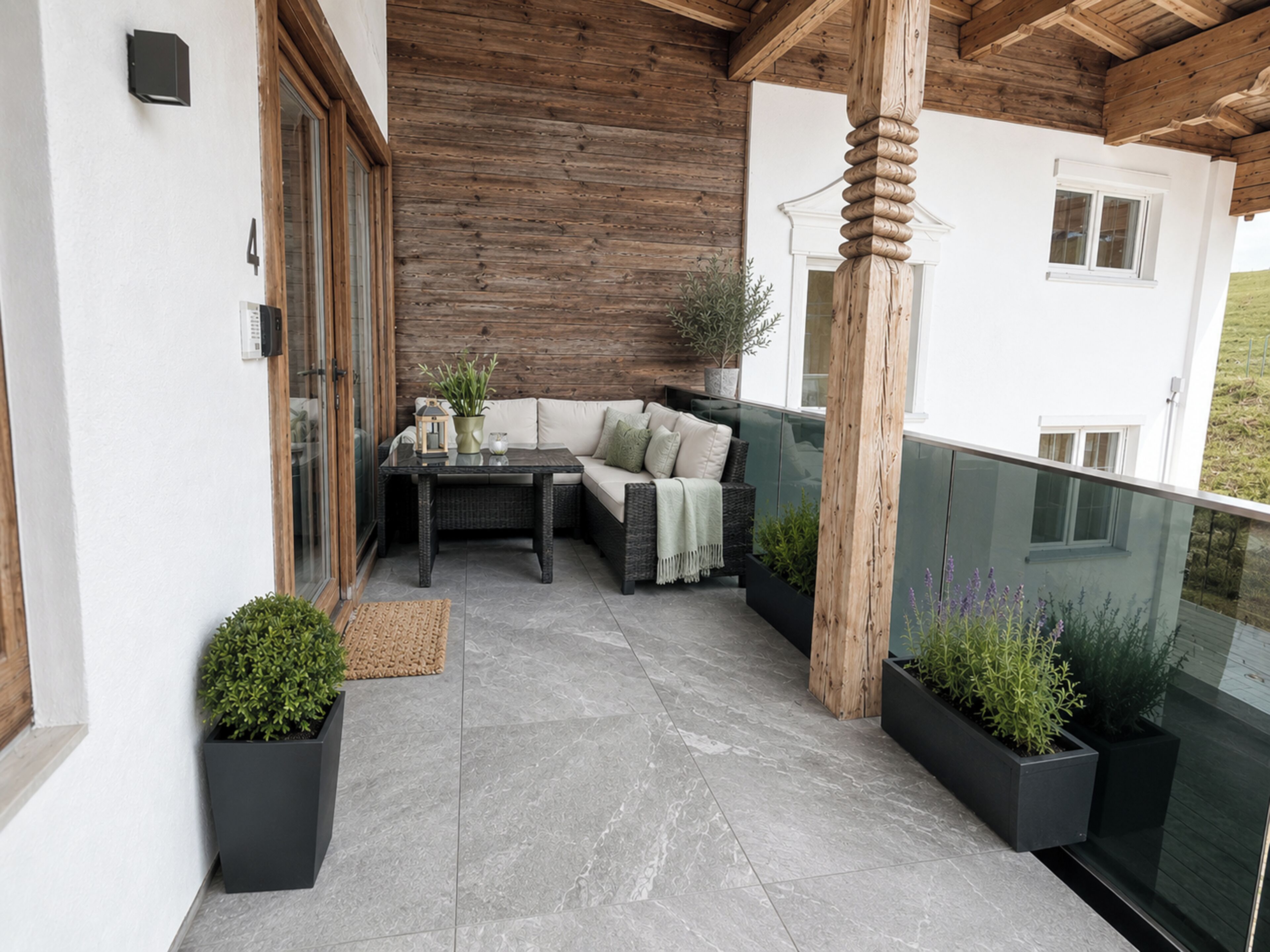 A balcony with a wicker sofa, a table, and potted plants.