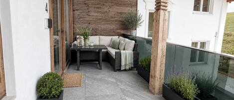 A balcony with a wicker sofa, a table, and potted plants.