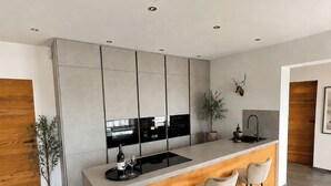 A modern kitchen with a central island, bar stools, and a wooden accent wall. - Apartment Katarina (Fieberbrunn)