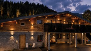 A modern log cabin with a stone facade, multiple windows, and a balcony overlooking a forested area. - Apartment Katarina (Fieberbrunn)