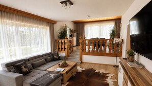 A modern living room with a sectional sofa, a coffee table, a large TV, and a staircase leading to an upper level. - Apartment Katarina (Fieberbrunn)