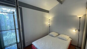 A bedroom with a bed, two bedside lamps, and a window with a view of trees. - Charming house near the port with parking and pets allowed (Capbreton)