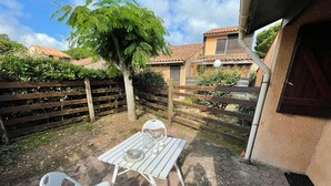 A patio with a table and two chairs, surrounded by a wooden fence and greenery. - Charming house near the port with parking and pets allowed (Capbreton)