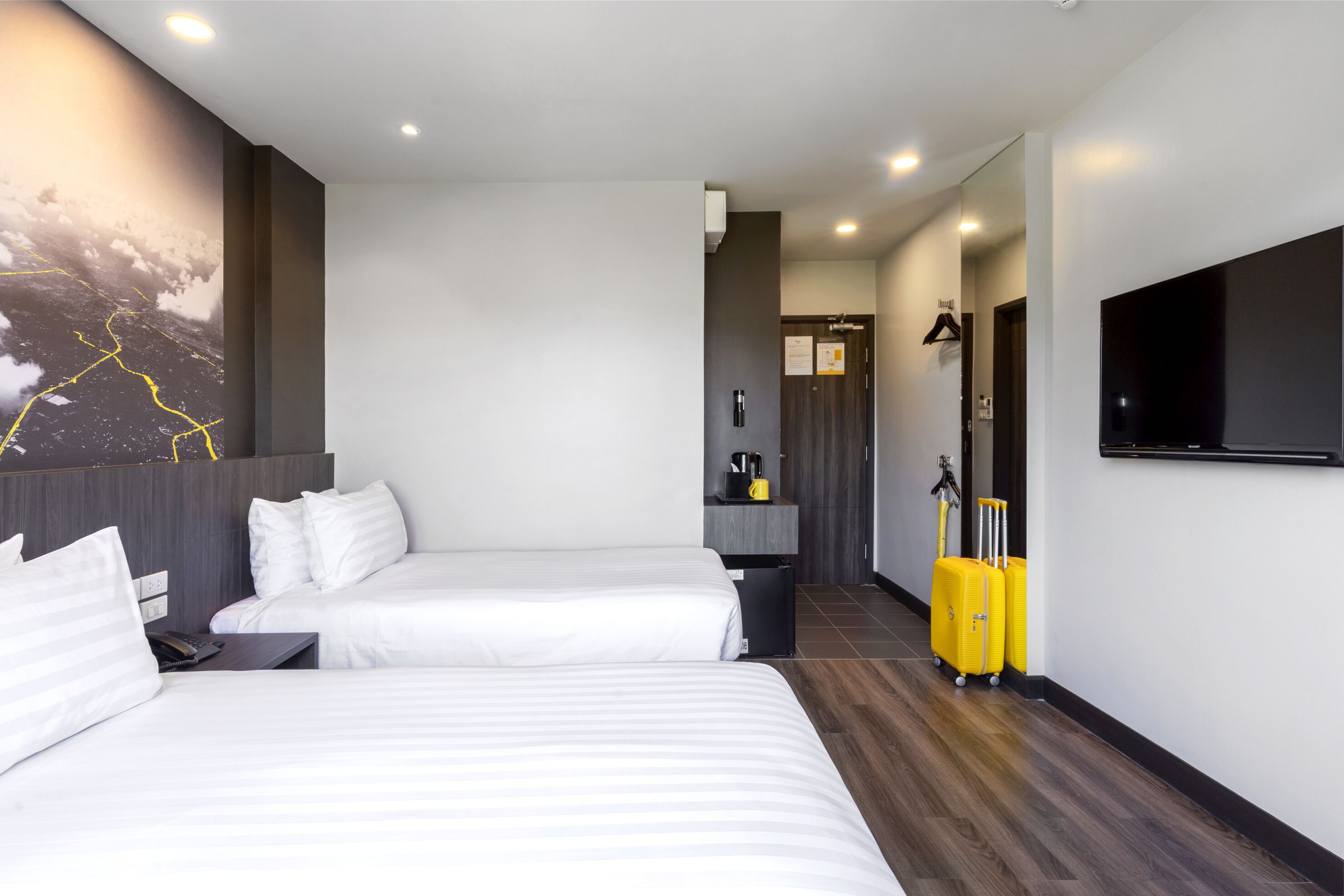 A hotel room with two beds, a flat-screen TV, a coat rack, and a wall-mounted heater.