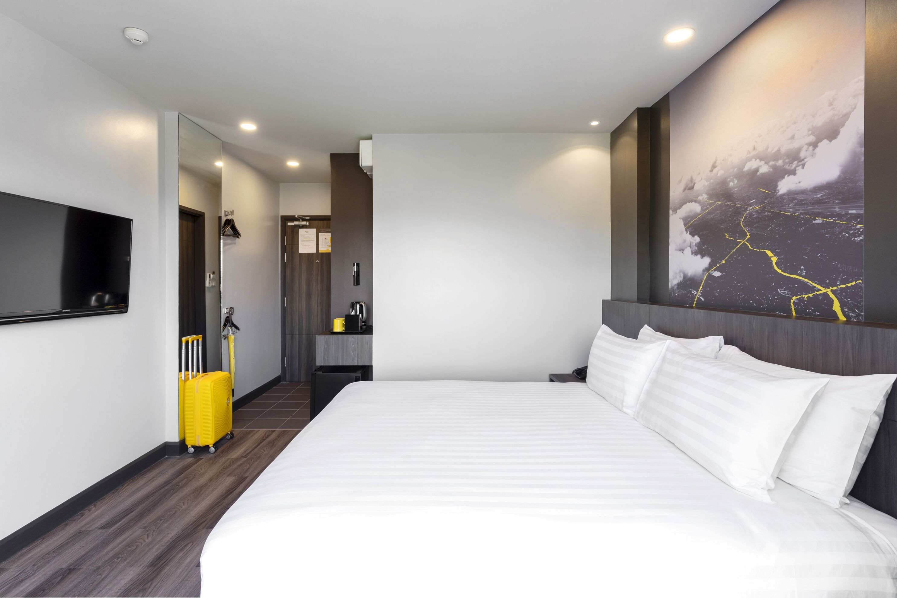 Habitación de hotel moderna con una cama grande, un televisor de pantalla plana, un escritorio y un baño visible a través de una puerta abierta.