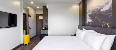Habitación de hotel moderna con una cama grande, un televisor de pantalla plana, un escritorio y un baño visible a través de una puerta abierta.