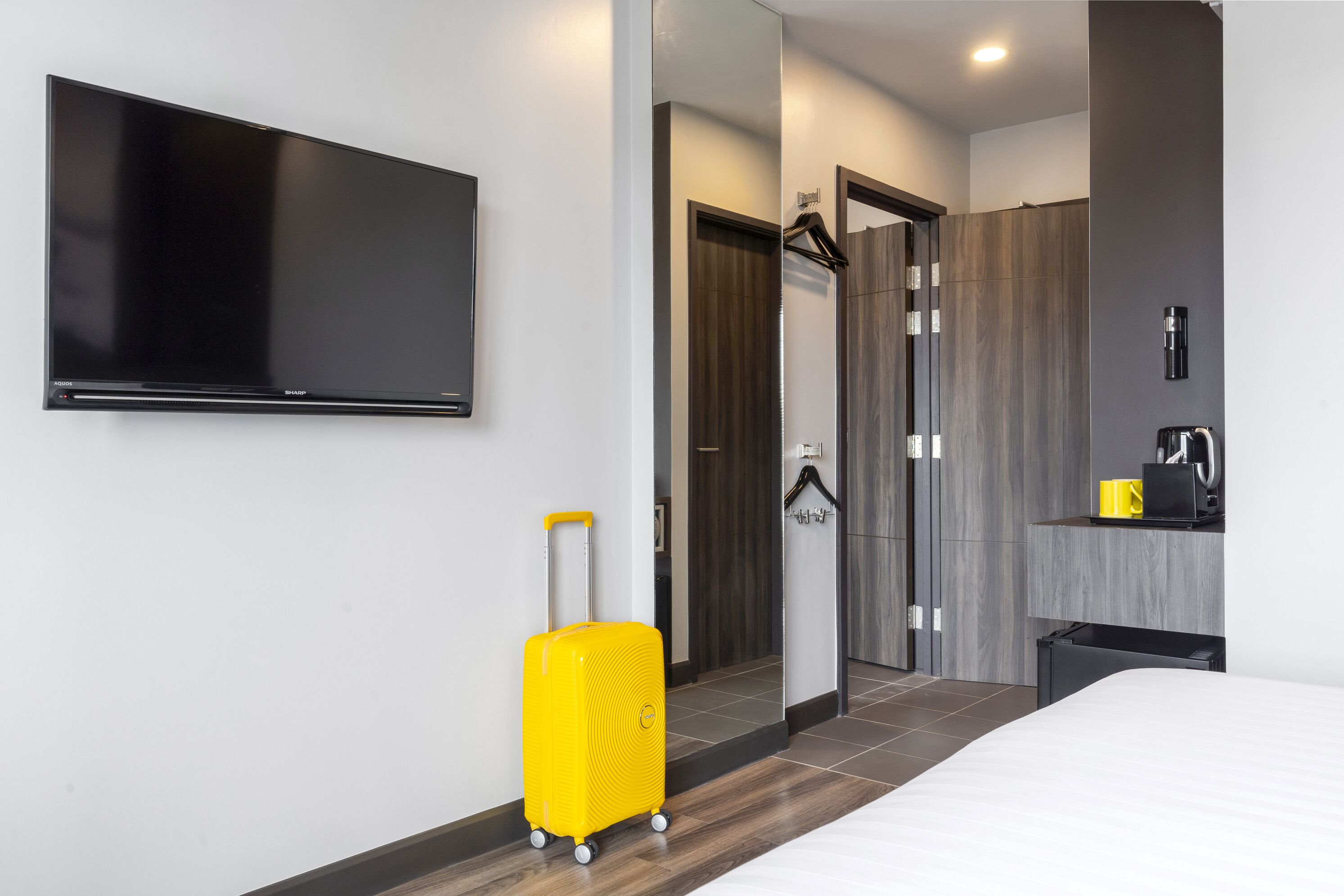 A hotel room with a bed, a television, a bathroom with a mirror, and a yellow suitcase.